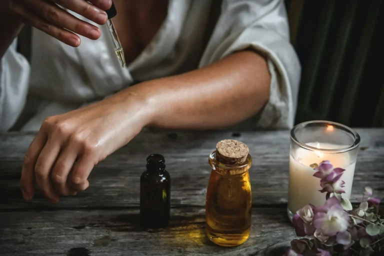 Application d'huile de soin sur le bras, flacons et bougie sur une table en bois